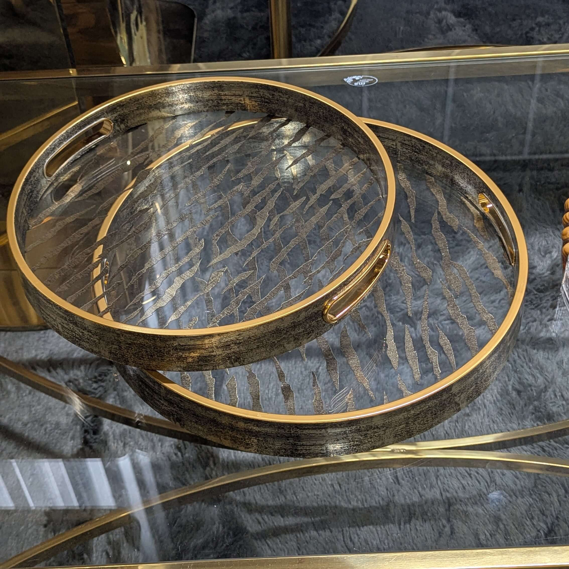 Vintage round serving tray with champagne gold details on a glass table, combines wood and sophisticated design for elegant serving.