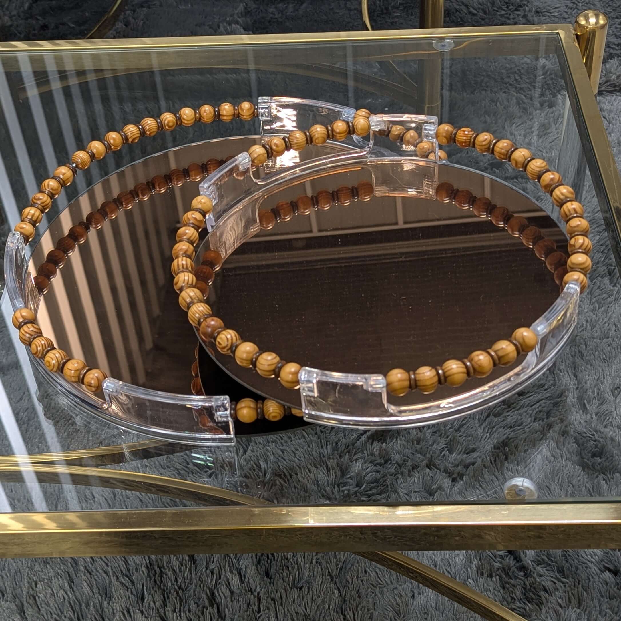 Round mirror serving tray set with wooden bead accents and metallic trim on a glass table.