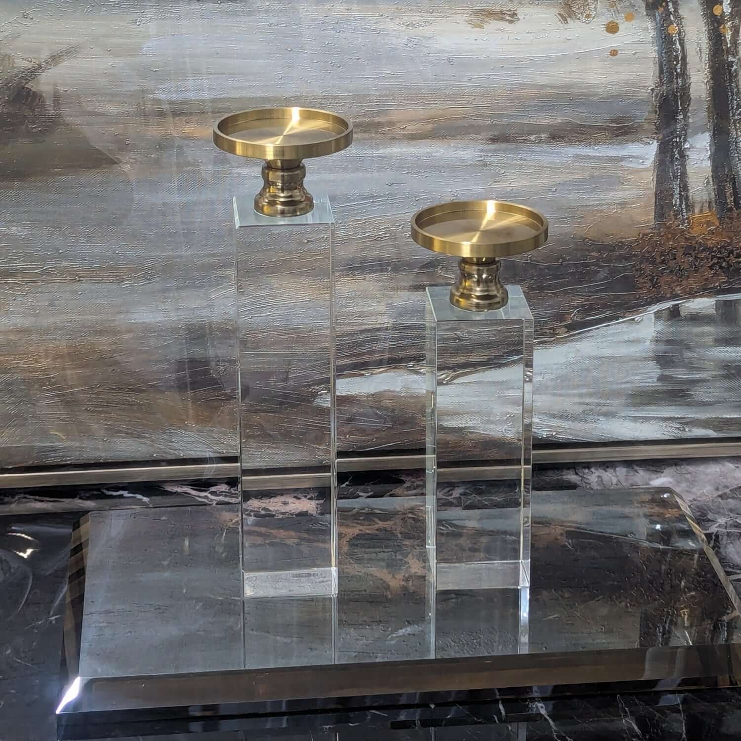 Two gold candle holders on clear stands against a marble background