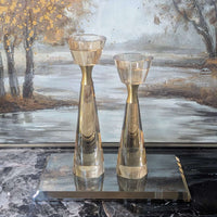 Two gold candle holders on a reflective surface with a decorative wall in the background