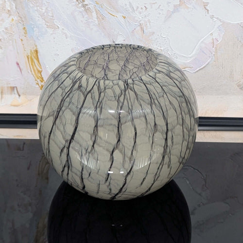 Spherical glass vase with textured surface against a abstract art background