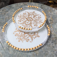 Elegant circular serving trays with decorative beading on a marble table, featuring intricate floral patterns and wood-plastic grips.