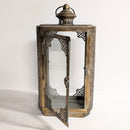 An antique-style lantern with a weathered bronze and gold-toned metal frame, featuring an open door with intricate filigree cutouts and a glass panel, set against a plain white background.