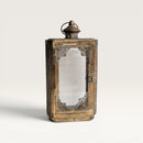 A vintage-style lantern with an ornate bronze metal frame, decorative corner filigree, and a clear glass front panel, shown on a light gray background.