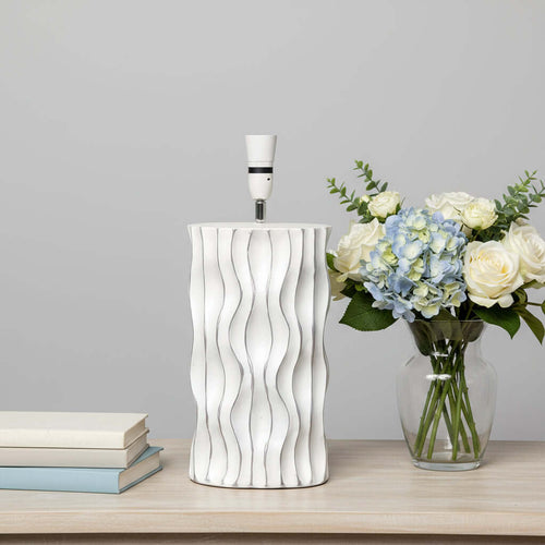Modern White Wavy Ceramic Lamp Base with elegant wavy texture on a wooden table, next to a vase of flowers and stacked books.